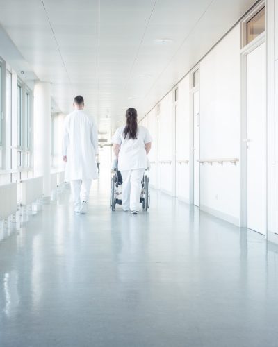 Doctor, nurse, and patient in wheelchair walking on hospital corridor